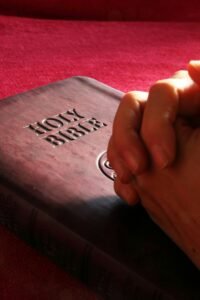 Close-up of hands praying on a Holy Bible, symbolizing faith and spirituality.