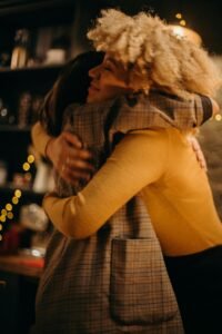 Two women hugging warmly indoors surrounded by festive lights.