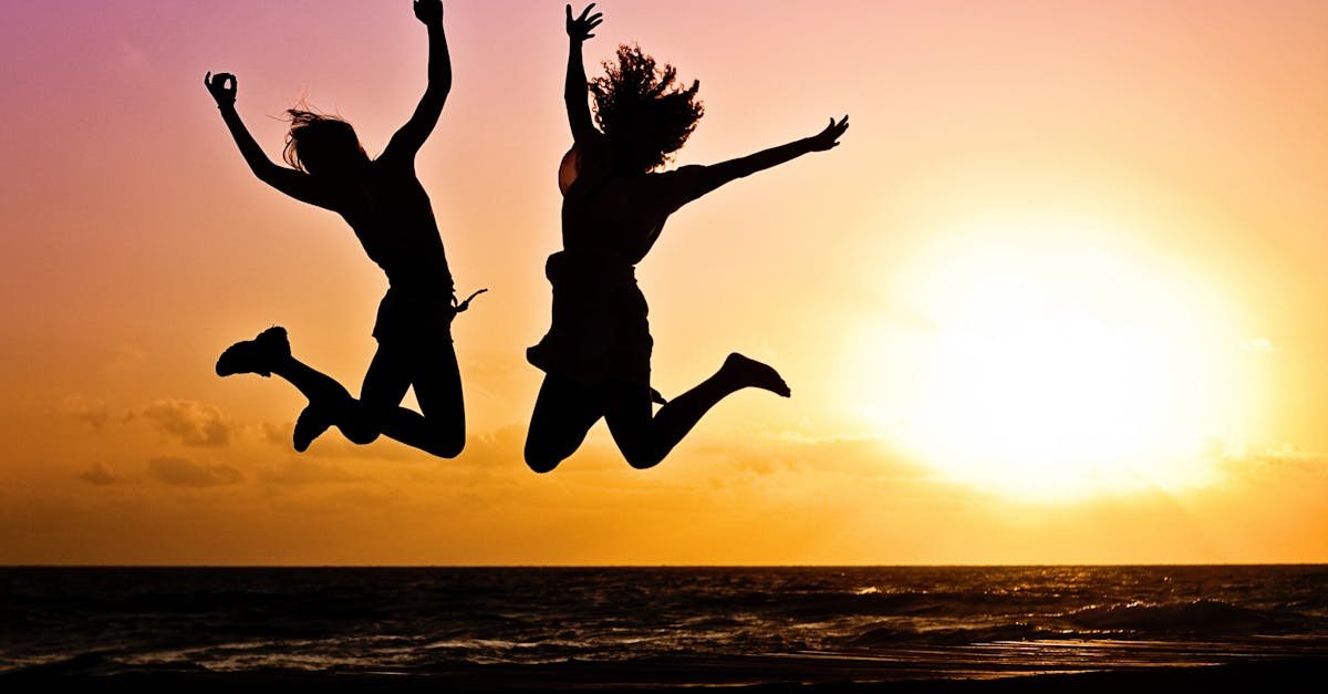 Silhouettes of two people joyfully jumping on a beach during a vibrant sunset.